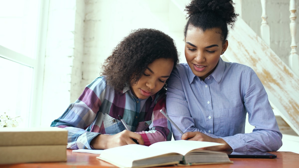 A parent and teenage daughter studying together from an open book