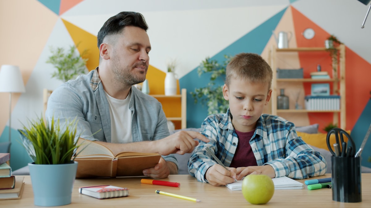 A parent pointing at a page while their child does homework at the table